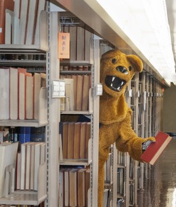 Nittany Lion mascot standing in Penn State library stacks holding book