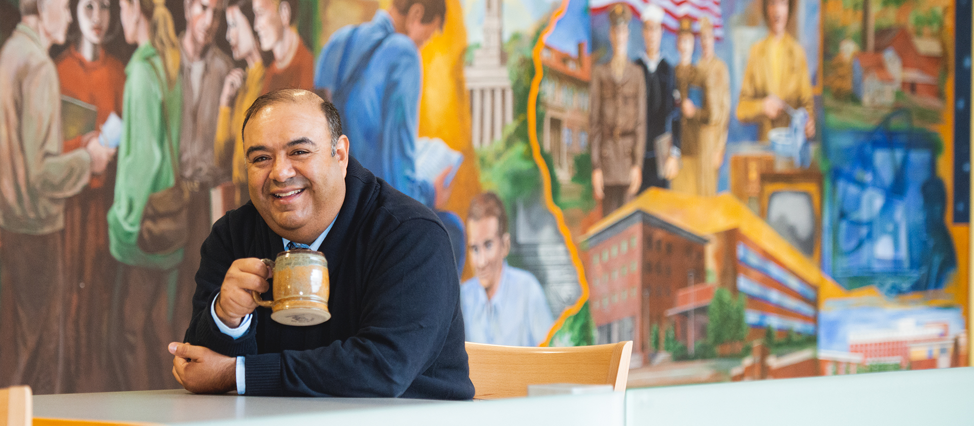 Smiling man holding coffee cup while sitting in front of colorful mural