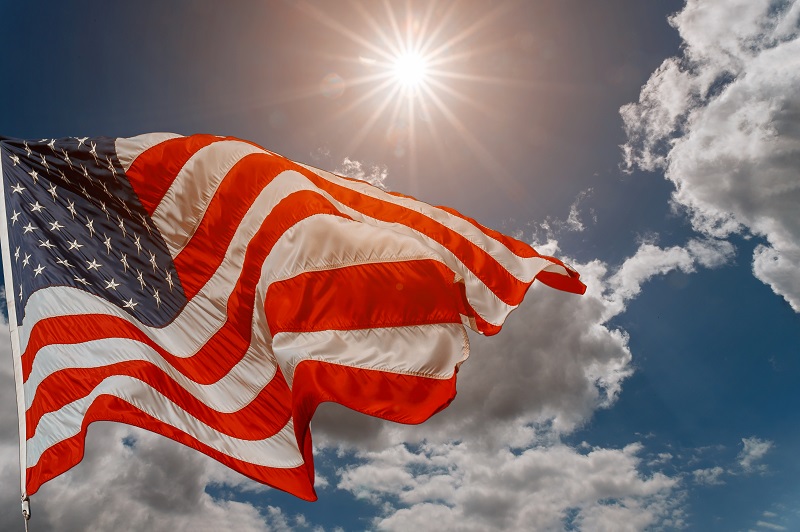 U.S. flag flying in front of sun and clouds