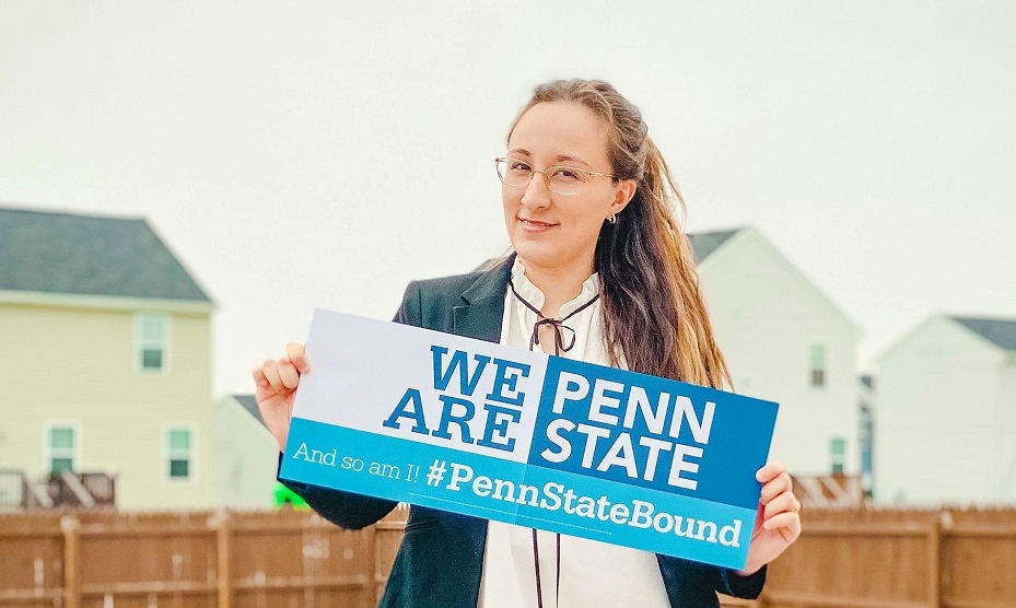 Woman with long hair and glasses holding sign saying "We Are Penn State"