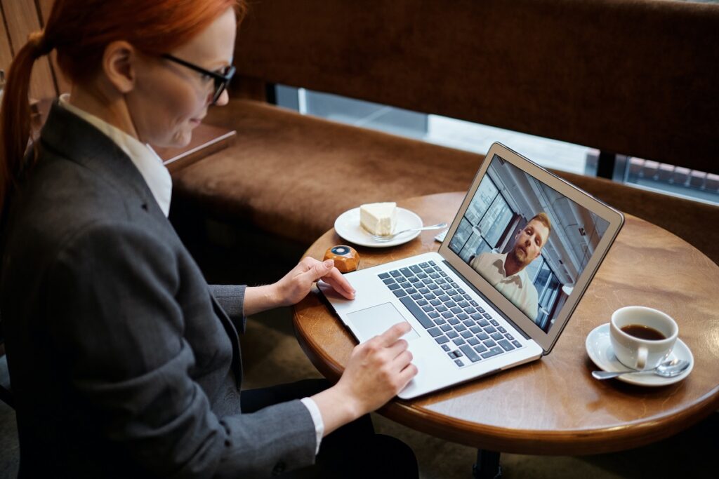 Woman using laptop and conducting virtual meeting with another person who appears on screen.