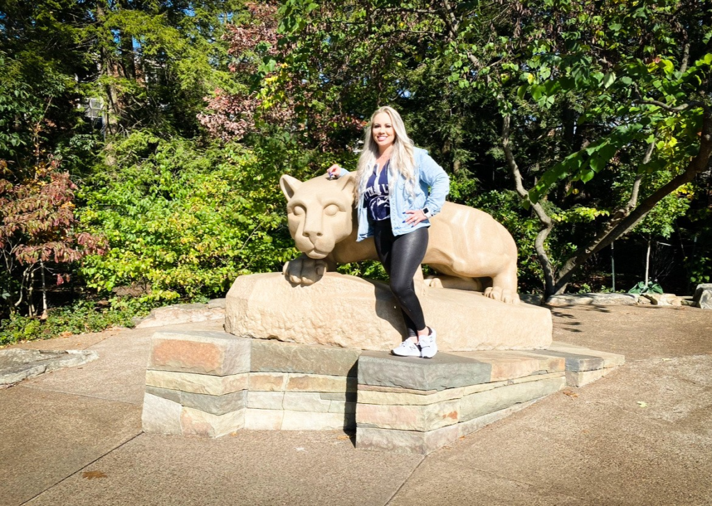 Smiling woman with long blonde hair standing next to the Nittany Lion Shrine.