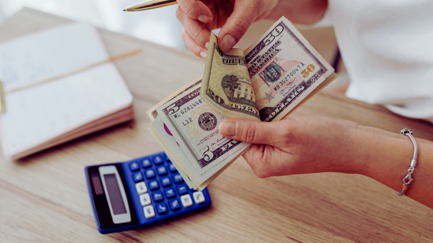 Hand holding paper currency of various denominations with a calculator visible nearby