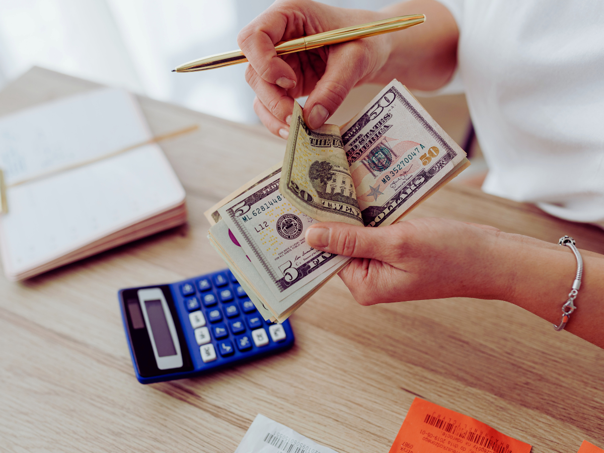 Hand holding paper currency of various denominations with a calculator visible nearby