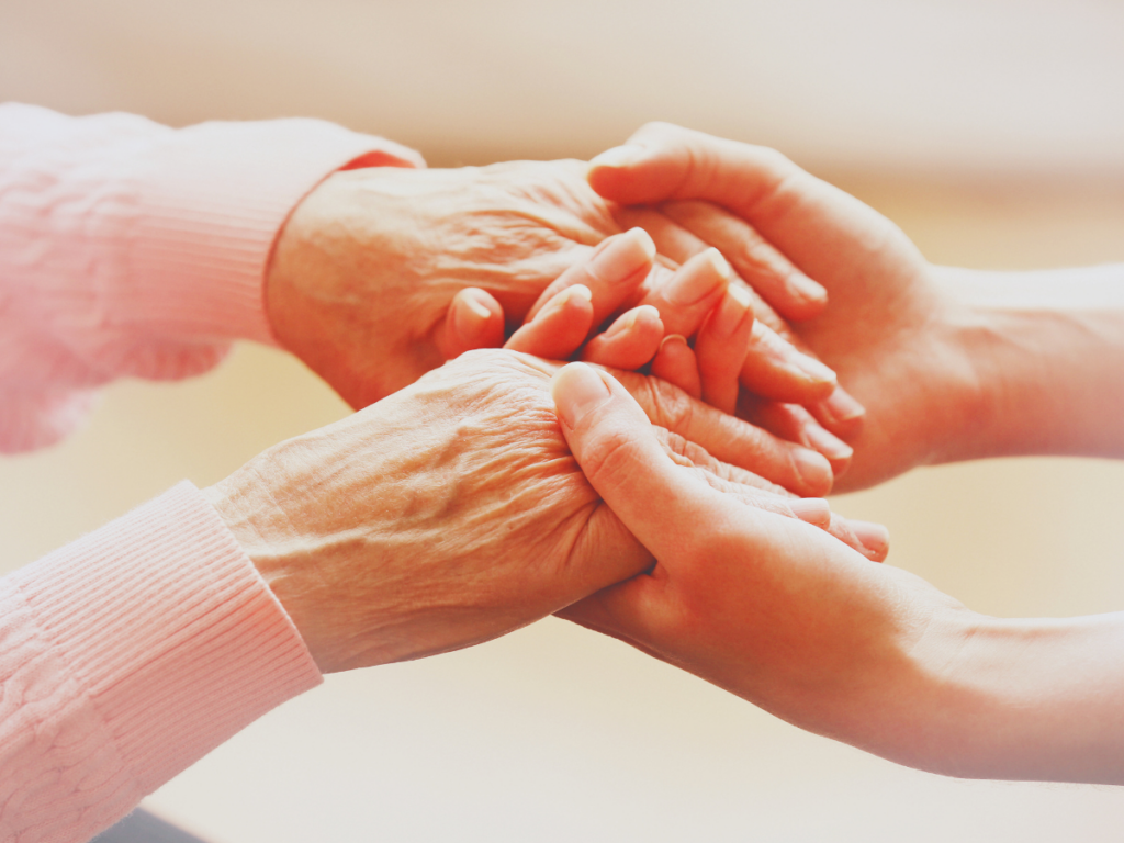 One pair of younger-looking hands holding hands that appear to be those of an older person