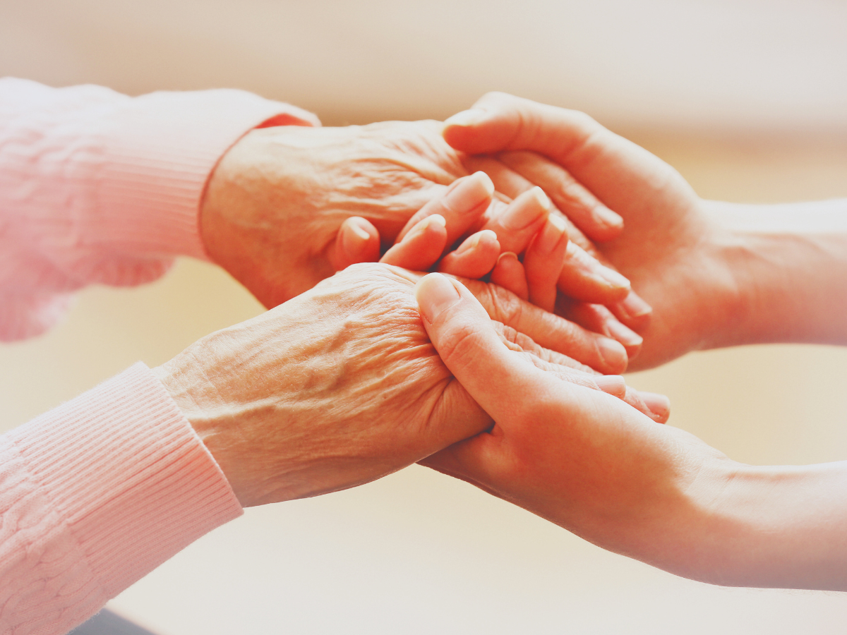 One pair of younger-looking hands holding hands that appear to be those of an older person