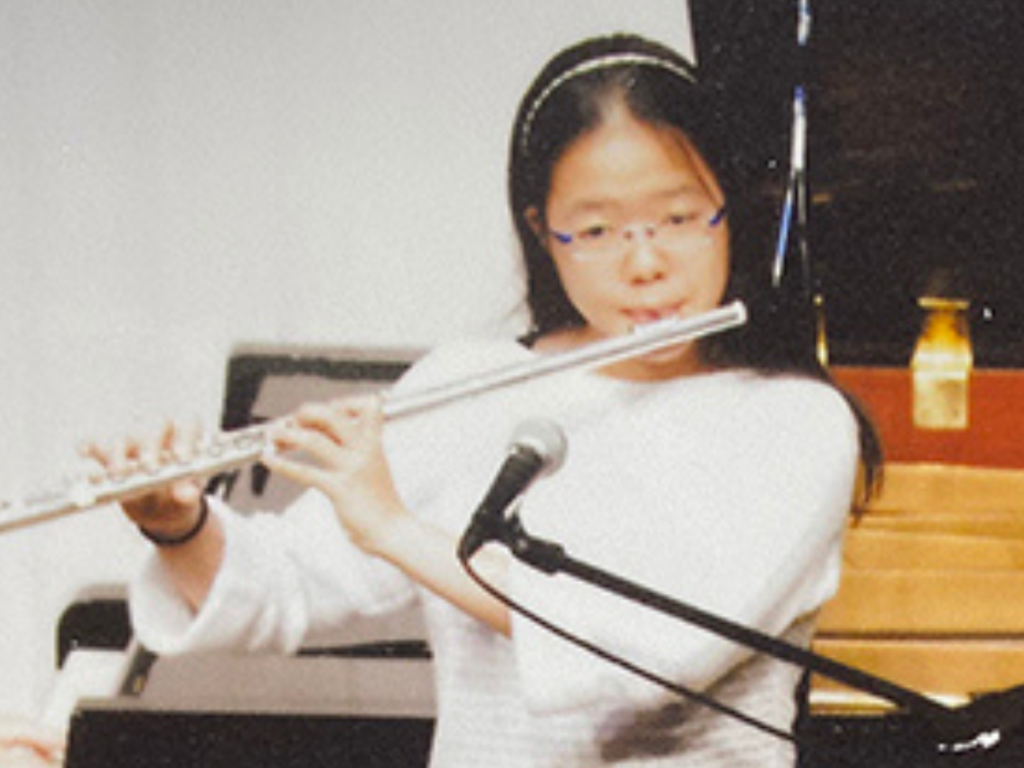 Japanese woman with long dark hair playing a wind instrument during what appears to be a concert or recital event