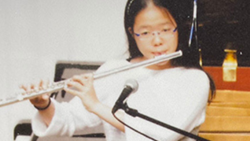 Japanese woman with long dark hair playing a wind instrument during what appears to be a concert or recital event